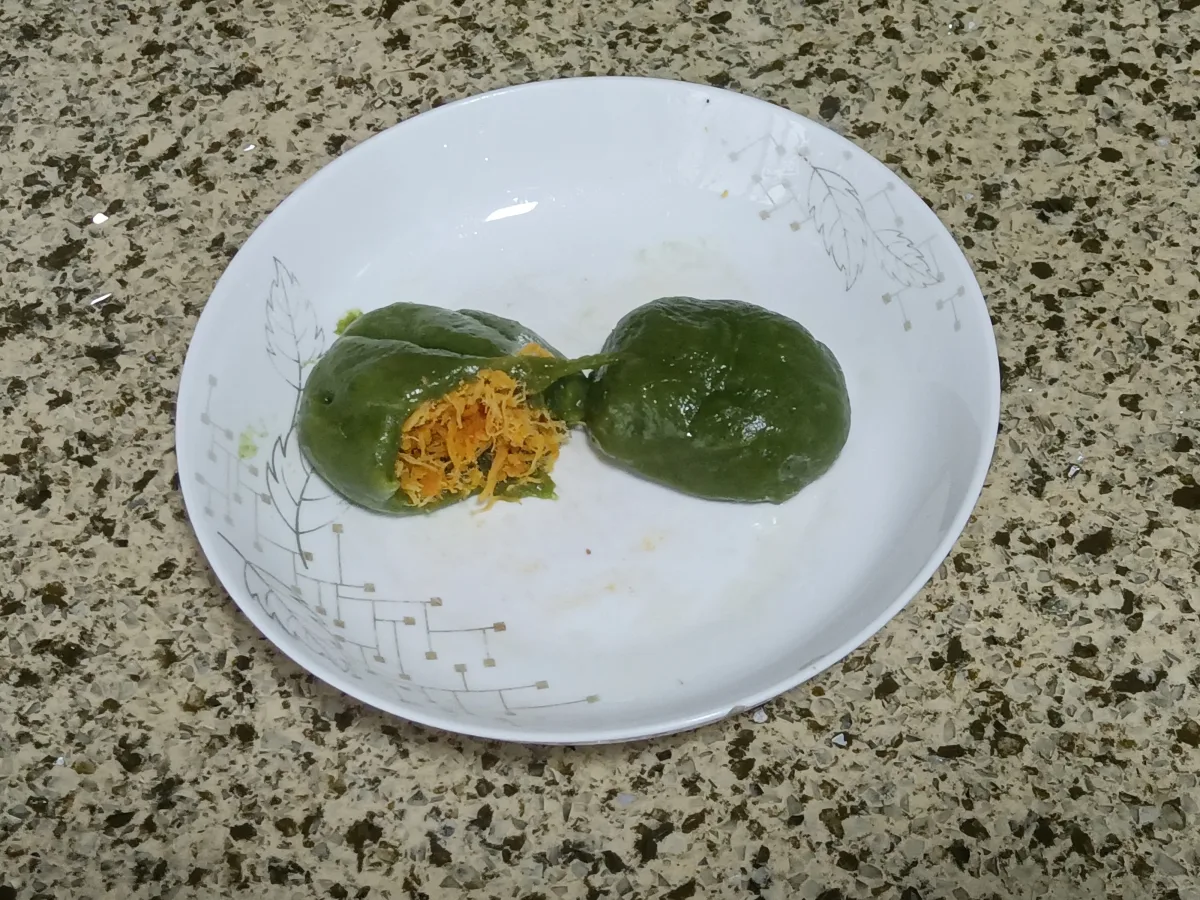 Two green qingtuan rice cakes on a plate, one opened to show its filling
