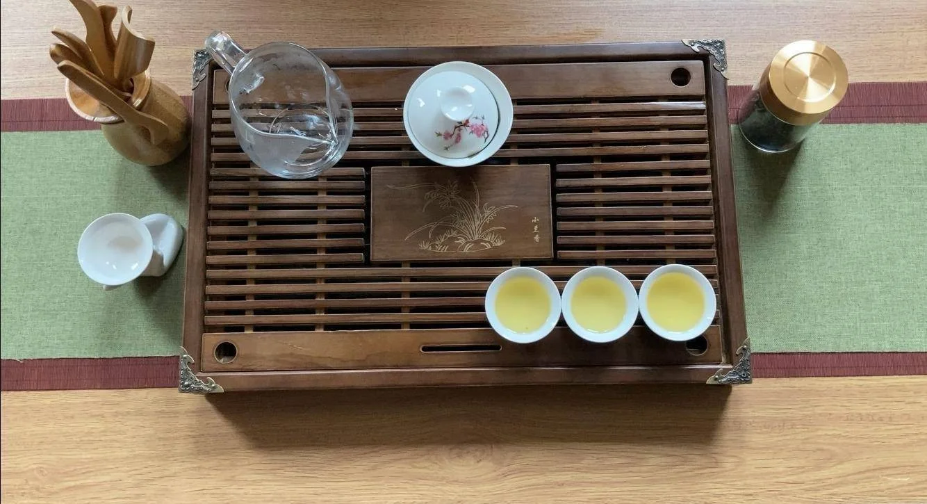 A gaiwan, glass serving pitcher and small teacups arranged on a wooden tea tray