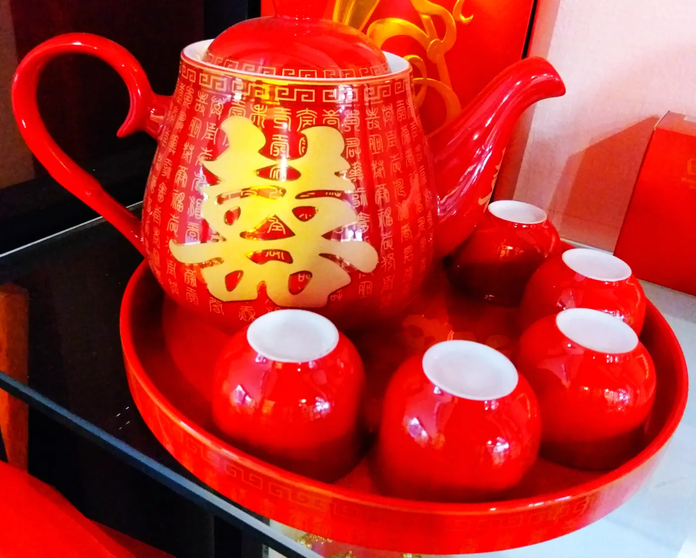 Red wedding teacups and a matching teapot arranged together on a round tray